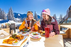 Zwei Frauen essen und trinken bei Sonne auf der Terrasse mit Blick auf schneebedeckte Berge. | © Hauser Kaibling