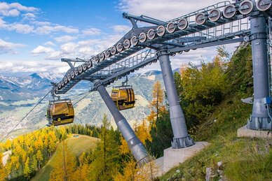 Gelbe Gondeln der Hochwurzenbahn fahren durch herbstlich gefärbten Wald mit Blick auf das alpine Tal. | © Alexander Klünsner