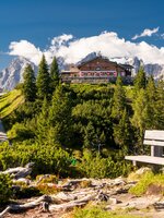Almhütte auf der Hochwurzen mit Terrasse, umgeben von Wald, Bergen und klarer Sommerluft unter blauem Himmel. | © Christine Höflehner