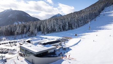 Blick auf die Talstation, Skifahrer und Gondeln, Wald und Berge im Hintergrund. | © Josh Absenger