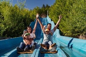 Zwei Erwachsene und zwei Kinder rutschen lachend nebeneinander eine blaue Wellenrutsche hinunter. | © Christine Höflehner