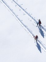Zwei Pistentourengeher mit Stöcken auf verschneiter Spur bei Sonne auf der Planai unterwegs | © Josh Absenger