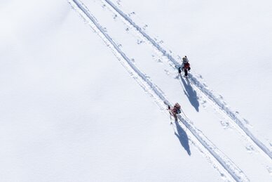 Zwei Pistentourengeher mit Stöcken auf verschneiter Spur bei Sonne auf der Planai unterwegs | © Josh Absenger