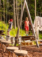 Two kids balance on wooden climbing elements at Hopsiland Planai, surrounded by forest and playful animal-shaped structures. | © Christine Höflehner