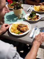 Grillteller mit Pommes, Salat und Getränken auf Holztisch im Sonnenschein, serviert auf einer Hütte auf der Planai im Sommer. | © Dietmar Körbler