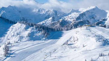 Schneebedeckte Pisten mit Sesselliften vor majestätischen Alpen und blauem Himmel. | © Josh Absenger