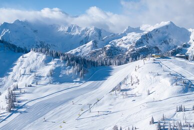 Schneebedeckte Pisten mit Sesselliften vor majestätischen Alpen und blauem Himmel. | © Josh Absenger