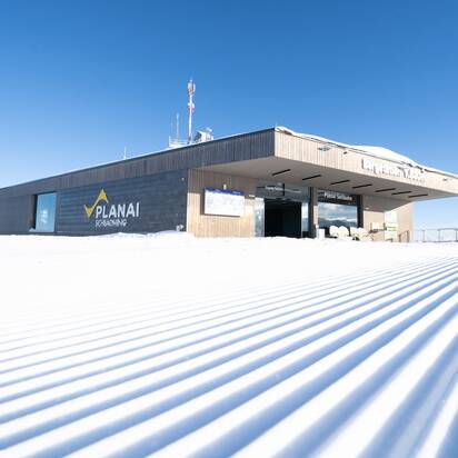 Planai-Bergstation mit glatter, frisch präparierter Skipiste vor Alpenkulisse. | © Josh Absenger