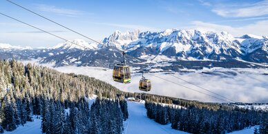 Zwei Gondeln fahren über verschneite Wälder vor majestätischen Alpen. | © Gerald Oberreiter