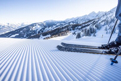 Skier auf einer frisch präparierten Piste vor verschneiter Alpenlandschaft. | © Mirja Geh