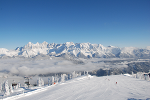Blick auf verschneite Piste, Skifahrer und beeindruckendes Bergpanorama im Hintergrund.