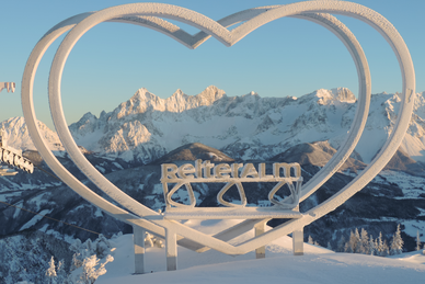 Steirerherz-Skulptur bei Reiteralm mit verschneitem Dachsteinmassiv im Hintergrund.