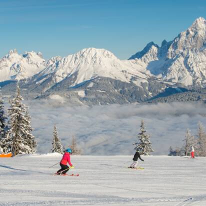 Zwei Skifahrer auf präparierter Piste der Reiteralm, mit verschneitem Dachsteinmassiv im Hintergrund. | © Lorenz Masser