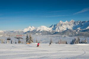 Zwei Skifahrer auf präparierter Piste der Reiteralm, mit verschneitem Dachsteinmassiv im Hintergrund. | © Lorenz Masser