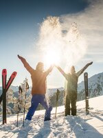 Zwei Skifahrer werfen Schnee in die Luft, Sonnenlicht, Berge, Skier und Stöcke im Schnee. | © Lorenz Masser