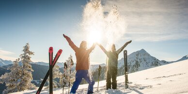 Zwei Skifahrer werfen Schnee in die Luft, Sonnenlicht, Berge, Skier und Stöcke im Schnee. | © Lorenz Masser
