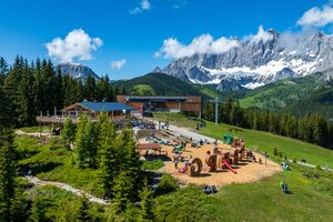 Weitläufiger Spielplatz mit Holzelementen, Rutschen und Kletterstrukturen vor einem Bergrestaurant und der Rittisberg-Seilbahn. | © Erlebnis Rittisberg