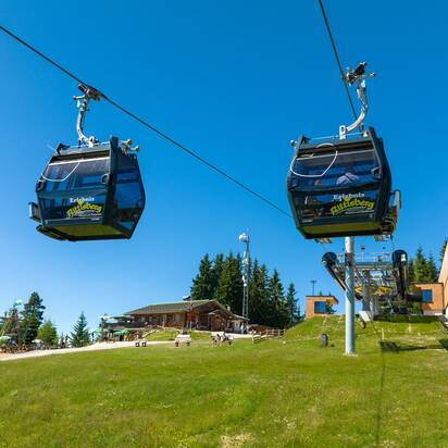 Zwei Gondeln der Rittisbergbahn erreichen die Bergstation, im Hintergrund Spielbereich, Hütten und blauer Himmel im Sommer. | © Rittisberg