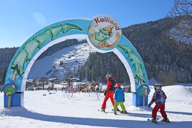 Three children skiing under colourful Kaliland archway in Ramsau