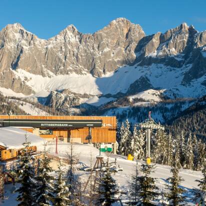 Rittisberg top station with hut, playground and Dachstein in sunlight.