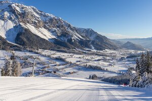 View from groomed ski slope of snowy Enns Valley and striking mountain backdrop.