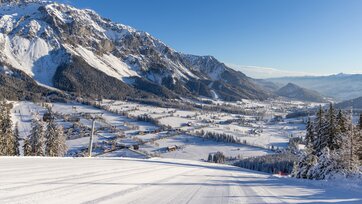 View from groomed ski slope of snowy Enns Valley and striking mountain backdrop.