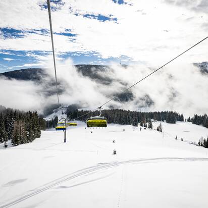 Gelber Sessellift fährt über verschneite Pisten und Wald in nebeliger Winterlandschaft | © filzmoos.ski