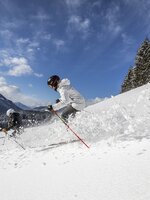 Zwei Skifahrer fahren bei Sonnenschein durch tiefen Pulverschnee am Waldrand | © filzmoos.ski