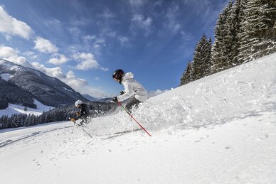 Zwei Skifahrer fahren bei Sonnenschein durch tiefen Pulverschnee am Waldrand | © filzmoos.ski