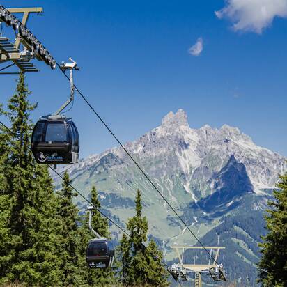 Papageno cable cars glide above conifer forest in Filzmoos, with a striking rocky mountain massif behind them. | © filzmoos.ski