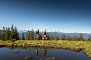 Two hikers in front of reflective water and Alpine panorama near Radstadt on a clear summer day | © Salzburger Sportwelt, Lorenz Masser