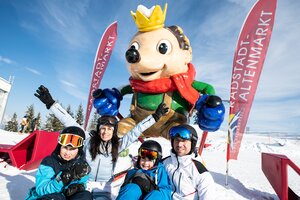 Familie sitzt vor einer Igelstatue mit Krone, die im Schnee steht