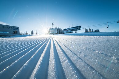 frisch präparierte Skipiste mit Blick von unten auf die Bergstationen der Liftanlagen