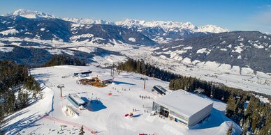 Plateau eines Skigebiets von oben mit drei Bergstationen und mehreren Skifahrern