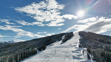 Skipiste umrahmt von Wald an einem schönen sonnigen Tag
