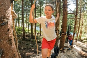 Girl balances on tires in a forest rope course, more kids climbing in the background. | © Shuttleberg