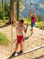 Girl balances on wooden beam in rope park, woman climbs in background. | © Shuttleberg