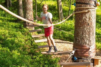 Mädchen überquert Hängebrücke im Waldseilgarten bei sonnigem Wetter. | © Shuttleberg