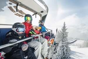 Vierköpfige Familie mit Skihelm und Brille auf Sessellift über verschneiter Winterlandschaft | © Shuttleberg