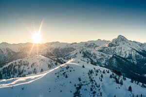 Verschneite Berglandschaft bei Sonnenuntergang mit Bäumen und Bergen im Hintergrund | © Markus Rohrbacher