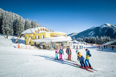 Eine kleine Gruppe von Kindern stehen auf der Piste und im Hintergrund ist ein gelbes Gebäude zu sehen | © Markus Rohrbacher