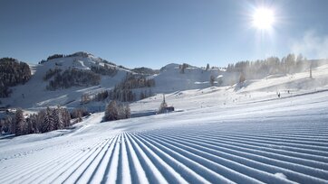 Perfekt präparierte Skipisten im Skigebiet Alpendorf mit Sonne, Schnee und Bergen