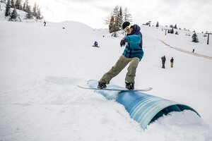 Snowboarder im Betterpark Alpendorf beim Rail-Slide, verschneite Piste und Zuschauer | © Gert Perauer