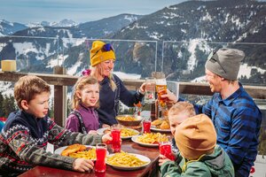 Eltern sitzen mit ihren vier Kindern auf der Terrasse einen Gasthauses und essen zu Mittag.  