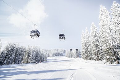 Achterjet Kabinenbahn Flachau mit Gondeln, verschneiten Tannen und präparierter Piste | © Snow Space Salzburg