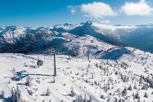 Schneebedeckte Berglandschaft mit wenig Bäumen von oben über die eine Gondelbahn fährt und eine Piste ist auch zu sehen  | © Snow Space Salzburg