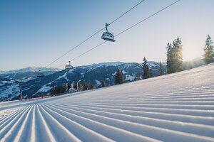 Perfekt präparierte Skipiste am frühen Morgen mit Sessellift und Bergen im Hintergrund | © Snow Space Salzburg