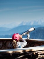Girl with red cap looks through telescope at alpine panorama from wooden viewing platform in Zauchensee mountains. | © Matthias Fritzenwallner