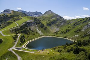 Reservoir lake with circular hiking path, play station and alpine scenery in the green summer mountains of Zauchensee