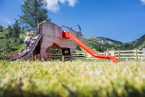 Mädchen erklimmt Kletterrampe eines Spielgeräts in Kuhform mit roter Rutsche am Spielplatz Zauchensee. | © Zauchensee Liftgesellschaft